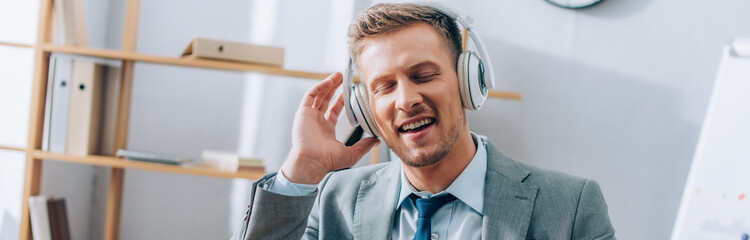 Positive businessman listening music in headphones in office, banner