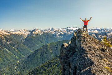 Hiker raises hands in celebration after reaching a mountain summit.