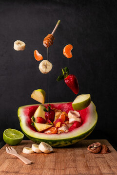 Composition of flying fruits falling on a bowl-shaped watermelon dippe