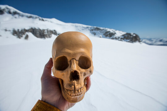 Man holds human skull, artifact in winter landscape.