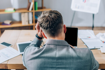 Obraz premium Back view of businessman sitting near devices and papers on blurred foreground