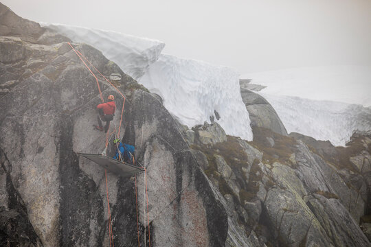 Climbers use rope to rappel onto portaledge on rock wall.