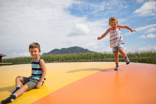Brother and sister enjoying time outdoors, jumping on trampoline.