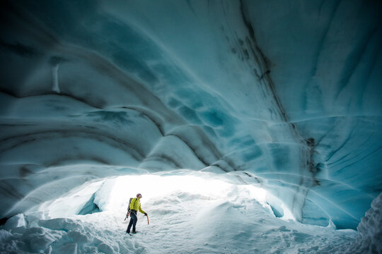 Ice climber looks up at the ceiling of a glacial ice cave in Canada.
