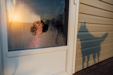 Girl wiping frost off window while dog shadow appears on house