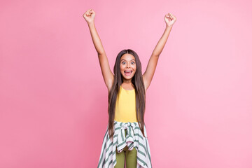Photo of little delighted girl raise fists successful goal isolated on pastel pink color background