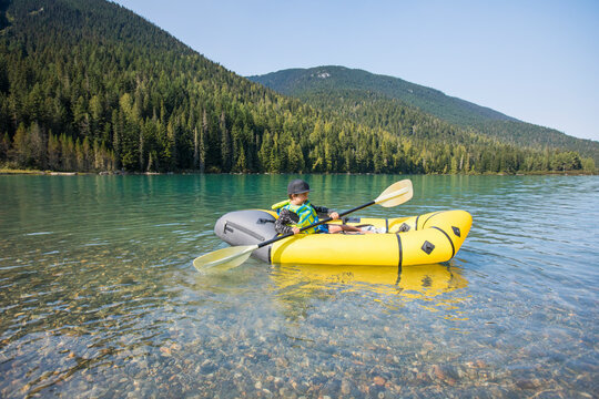 Young boy paddling yellow boat on scenic lake.