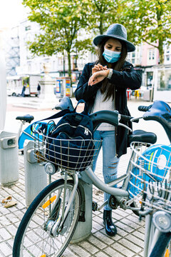 Young woman with mask chooses bicycle at a public rental point