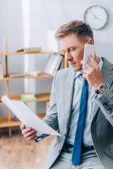 Naklejka premium Businessman in suit talking on smartphone while working with papers in office