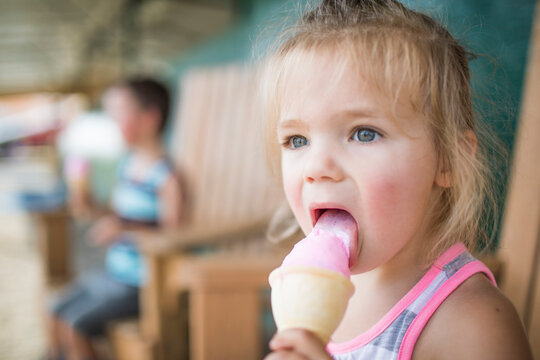 Young cute girl happily licking pink ice cream on summer day.