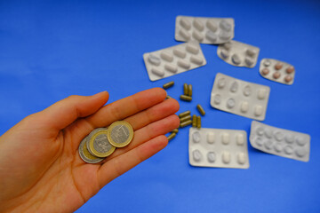 hand holding euro coin across pills, and capsules on blue background close-up. Finance, healthcare, medicine concept. Pricing, insurance, poverty