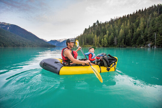 Father and son laughing, enjoying paddling trip on turquoise lake.