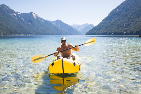 Shirtless man paddling inflatable packraft or kayak.