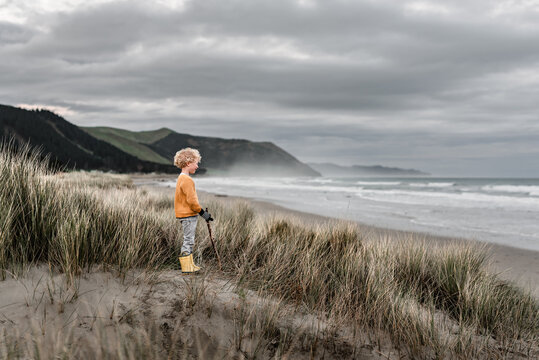 Blond curly haired boy watching ocean on cloudy day in New Zealand