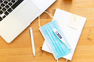 work supplies and means of prevention of coronavirus. laptop notepads and medical mask thermometer on wooden background. work during pandemic concept.