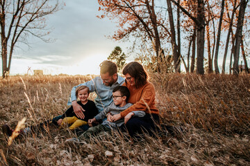smiling young family snuggling in a field on a fall evening