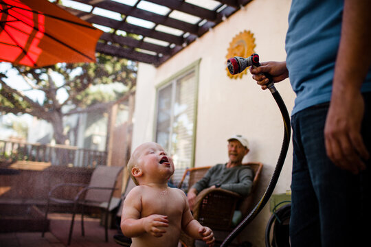 Uncle Spraying Nephew with Hose as Grandpa Smiles in San Diego