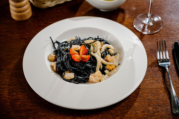 Black spaghetti. Spicy Black seafood pasta with squid with basil on wooden table.