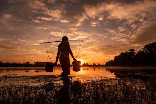 SRA SRANG,ANGKOR PARK, SIEM REAP, CAMBODIA - 17 August 2014: Local lady collects water in buckets over the shoulder for her garden from angkorian bathing pool.