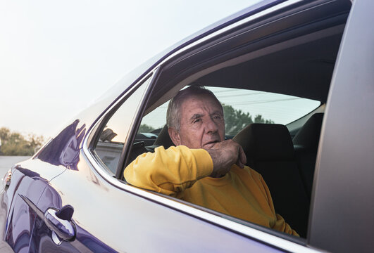 An old man sitting in the back seat of an electric car