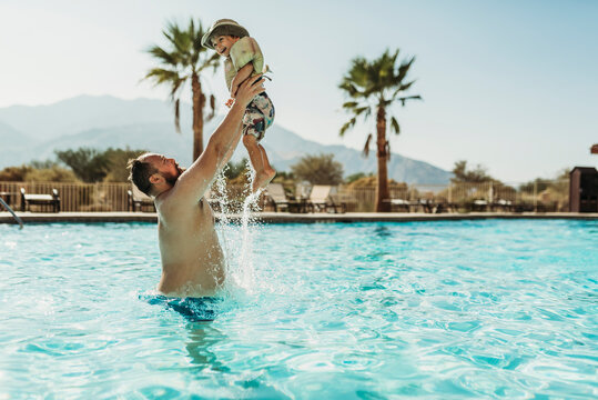 Father throwing young boy up in air while playing in pool on vacation
