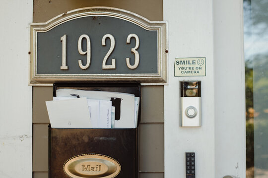 Front of house with overflowing mailbox, camera, and doorbell