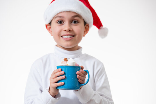 A boy in a red santa hat smiles and holds a cup of marshmallows. Christmas concept.