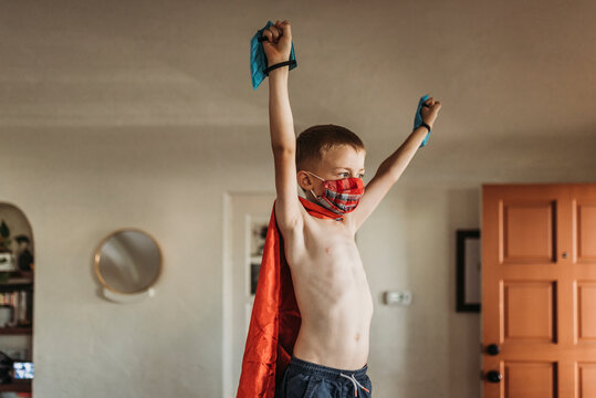 Young boy with arms outstretched wearing superhero costume and mask