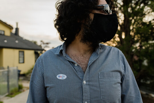man wearing face mask and sunglasses with 'I voted by mail' sticker