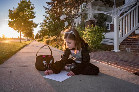 A young girl in a cat costume writes a note to the toothless fairy