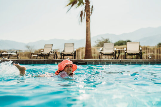 Side angle view of little girl in pink hat swimming in pool