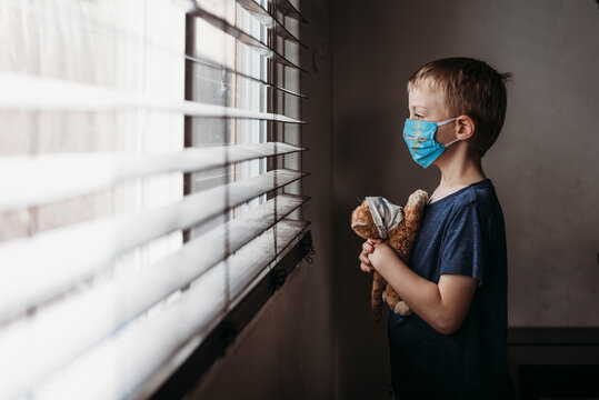 Side view of young school aged boy with mask on with stuffed animal
