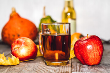 Glass of apple cider with apples, pumpkins and persimmon on wooden table