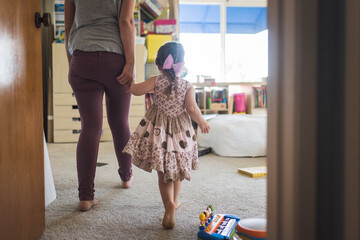 Barefoot mom and daughter holding hands walking into child's bedroom