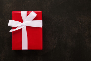 Top view of Christmas gift box wrapped with red paper and white ribbon on grunge background.