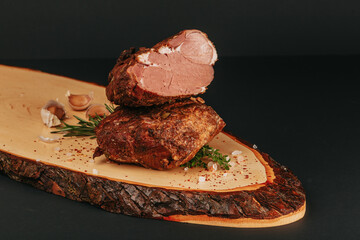 Smoked pork muscles and bacon on a wooden board with the addition of fresh aromatic herbs, garlic, sea salt and pepper.