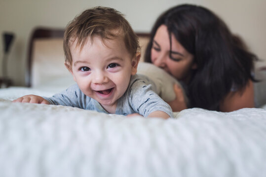 Laughing year old baby on stomach on bed with playful mid-30's mother