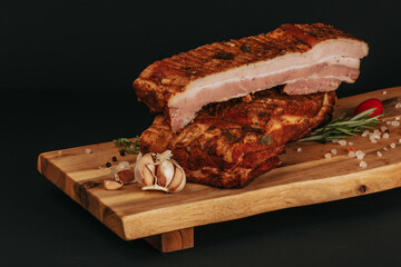 Smoked pork muscles and bacon on a wooden board with the addition of fresh aromatic herbs, garlic, sea salt and pepper.