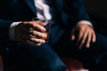 The groom, the businessman sits and holds a glass of whiskey. Preparing the groom for the wedding morning. Close-up