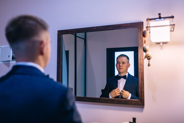 a man looks in the mirror and fixes his jacket.
