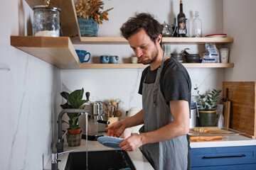 Profile side view portrait of serious concentrated guy housekeeper cleansing plates at light white modern style interior. Scandinavian kitchen and dishes