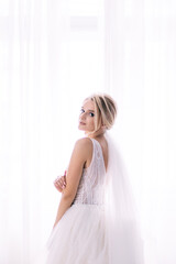 Fototapeta premium Young bride posing in wedding dress at home. Perfect makeup and hairstyle. Preparing the bride at home