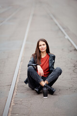 beautiful long-haired brunette in leather jacket sits on tram tracks