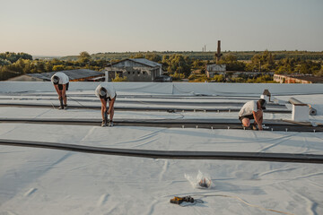 Construction worker drill with a powerful electric drill synthetic membrane for a new roof. © Doralin