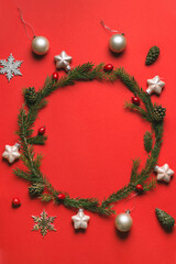 Fototapeta na wymiar Wreath of fir, pine cones, rowan berries, balls and gift boxes on red background. Winter design. Flat lay