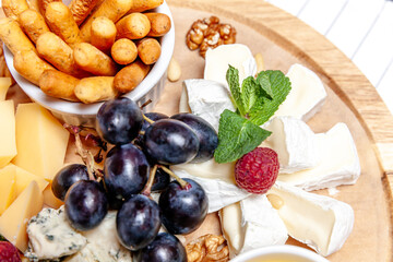 Board with different types of cheese. Cheeses mix set dor blu chedar parmesan brie honey sauce finger bread and grape on wooren palte. Restaurant menu breakfast plate. Healthy snack assortment.