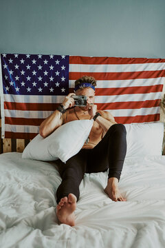 A young man taking pictures in bed with the American flag behind