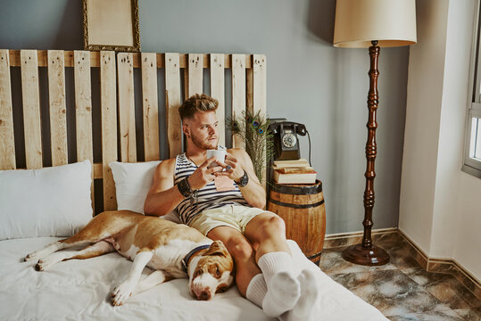 A young blond boy with a cup of coffee and his dog in bed