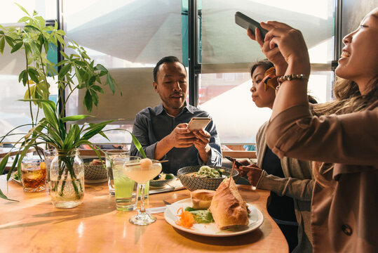 Three friends taking cell phone photos of food at Asian restaurant
