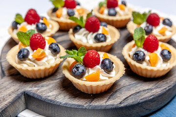 Fruit and berry tartlets dessert assorted on wooden tray. Closeup of delicious pastry sweets pies colorful cakes with fresh natural raspberry blueberry and cheese cream. French bakery catering.